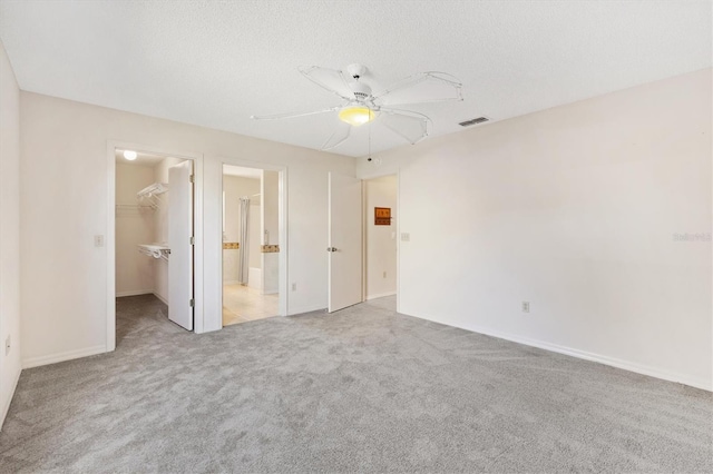 unfurnished bedroom featuring a walk in closet, ceiling fan, a textured ceiling, light colored carpet, and a closet