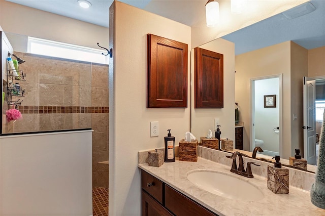 bathroom with a tile shower, vanity, and toilet