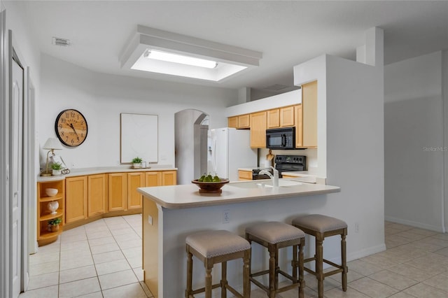 kitchen with kitchen peninsula, light tile patterned floors, light brown cabinets, and black appliances