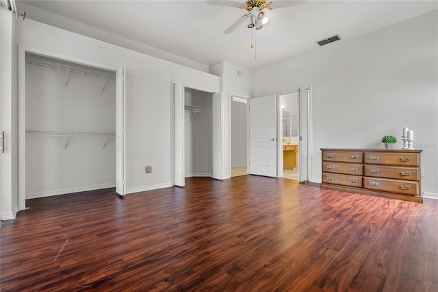 unfurnished bedroom with multiple closets, ceiling fan, connected bathroom, and dark wood-type flooring