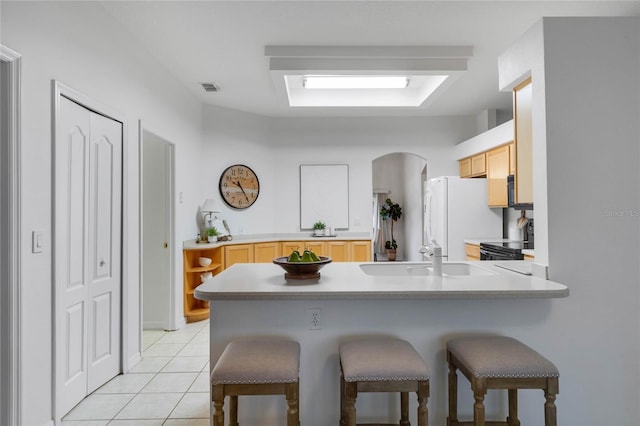 kitchen with light tile patterned flooring, sink, a kitchen bar, white fridge, and black range with electric stovetop