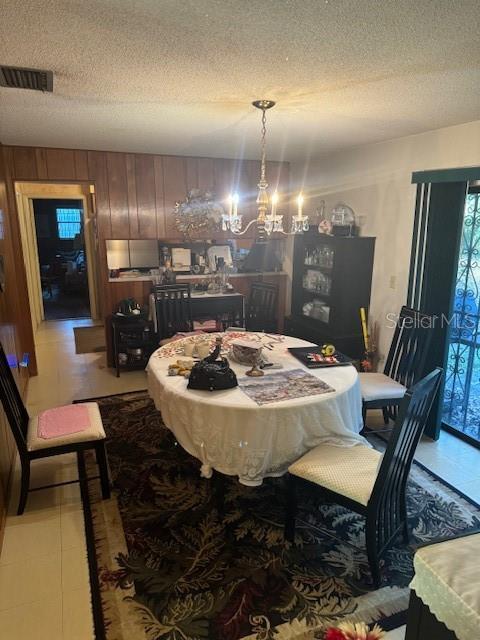 dining area featuring wood walls, light tile patterned flooring, a textured ceiling, and a chandelier