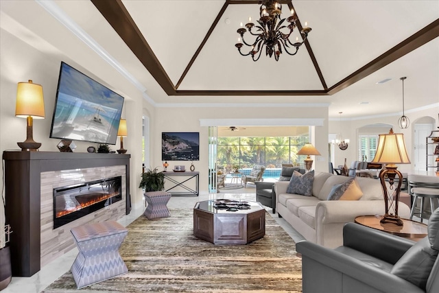 living room with a tiled fireplace, ornamental molding, a tray ceiling, and a chandelier