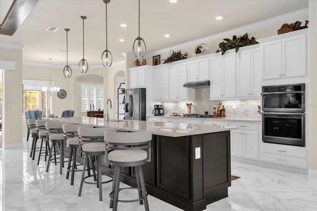 kitchen featuring a large island with sink, white cabinets, hanging light fixtures, ornamental molding, and stainless steel appliances