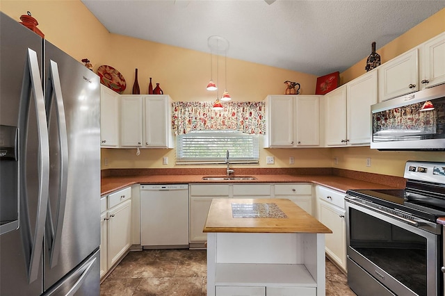 kitchen featuring lofted ceiling, sink, decorative light fixtures, white cabinetry, and stainless steel appliances