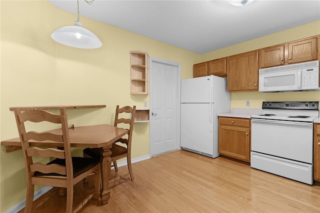 kitchen with light wood-type flooring, a textured ceiling, white appliances, and hanging light fixtures