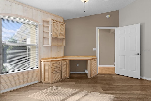 unfurnished office with wood walls, wood-type flooring, a textured ceiling, lofted ceiling, and built in desk