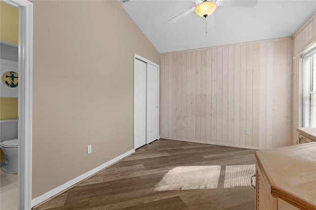 unfurnished bedroom with dark hardwood / wood-style flooring, vaulted ceiling, ceiling fan, and wood walls