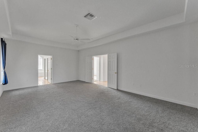 carpeted empty room with a raised ceiling and ceiling fan