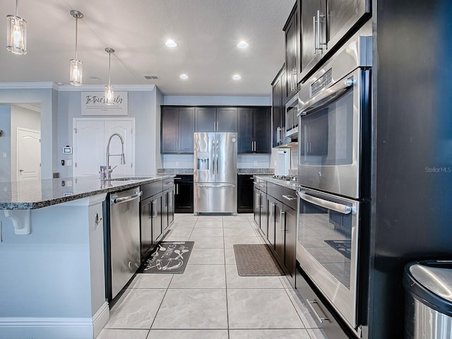 kitchen with sink, stainless steel appliances, an island with sink, decorative light fixtures, and a kitchen bar