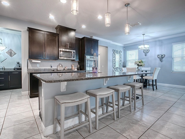 kitchen with pendant lighting, an island with sink, stainless steel appliances, and dark brown cabinets