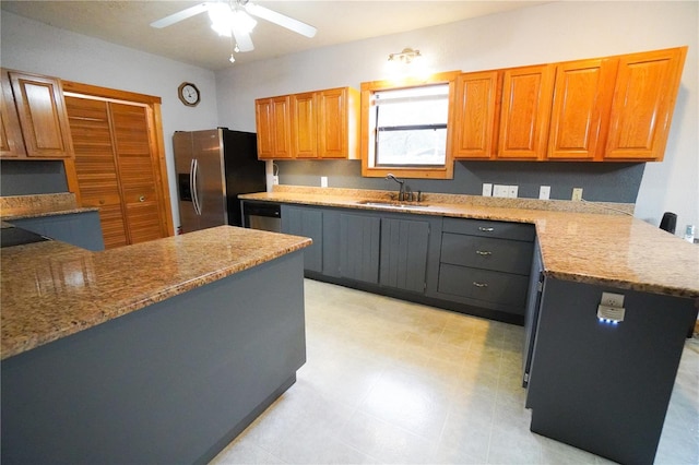 kitchen featuring light stone countertops, a center island, stainless steel appliances, ceiling fan, and sink