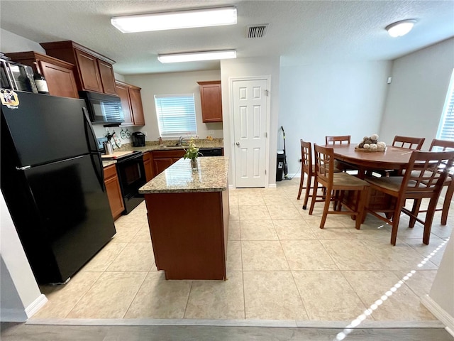 kitchen with a center island, black appliances, sink, light stone countertops, and a textured ceiling