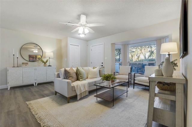 living room with a textured ceiling, ceiling fan, and dark wood-type flooring