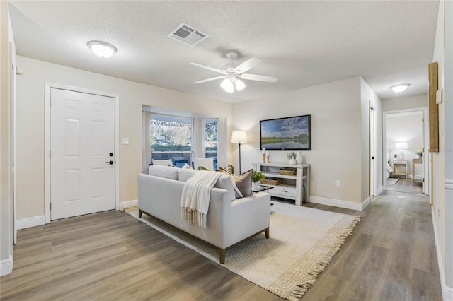 living room with hardwood / wood-style flooring, ceiling fan, and a textured ceiling