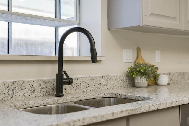 interior details featuring light stone counters, sink, and white cabinets