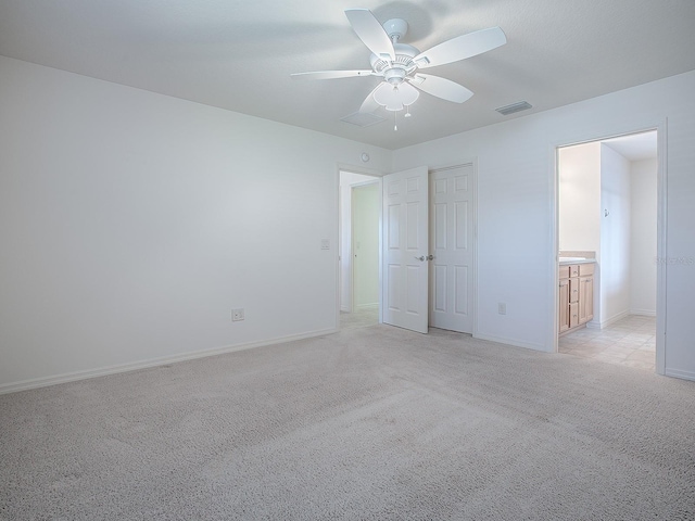 unfurnished bedroom featuring ceiling fan, light colored carpet, and ensuite bath