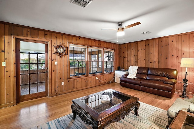 living room featuring ceiling fan, wood walls, and light hardwood / wood-style flooring