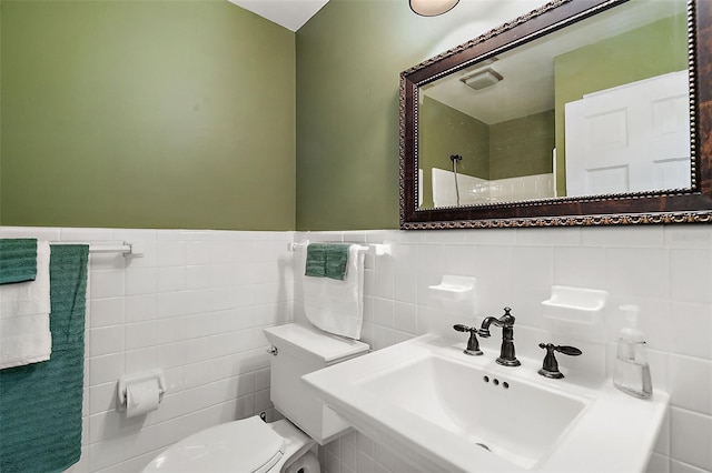 bathroom with toilet, sink, and tile walls