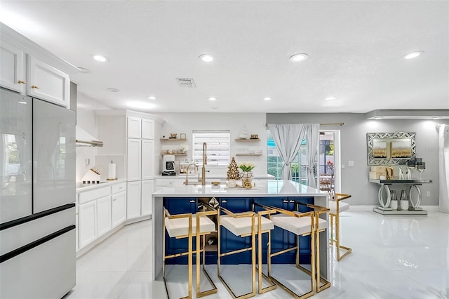 kitchen with a center island with sink, a breakfast bar, light tile patterned flooring, and white cabinetry