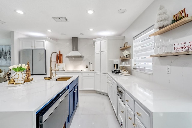 kitchen with white cabinets, wall chimney range hood, decorative backsplash, light stone countertops, and stainless steel appliances