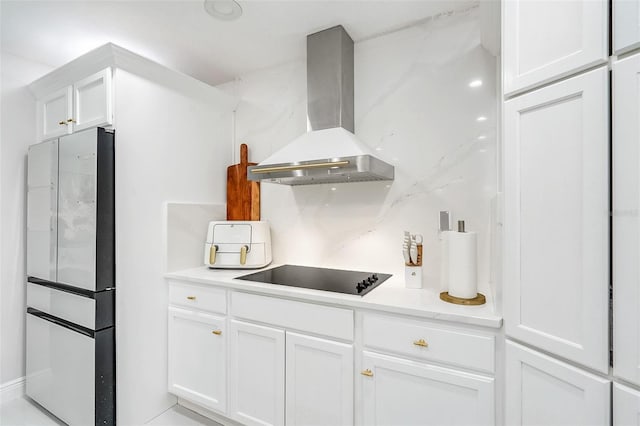 kitchen with black electric stovetop, backsplash, wall chimney range hood, white cabinets, and stainless steel refrigerator