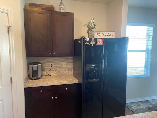 kitchen featuring dark brown cabinets, backsplash, black fridge, and a healthy amount of sunlight