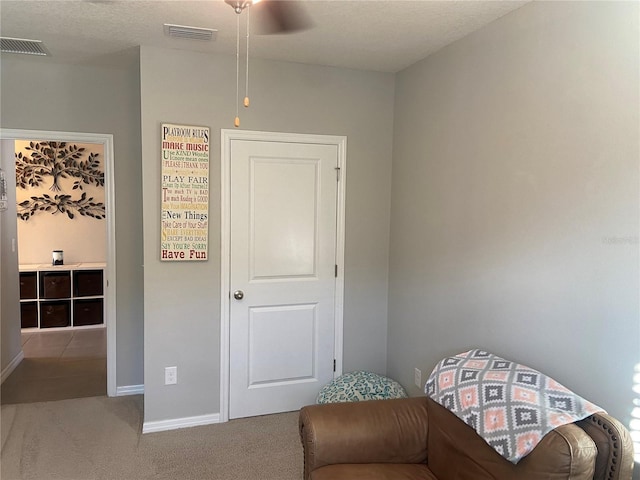 living area with ceiling fan, carpet, and a textured ceiling