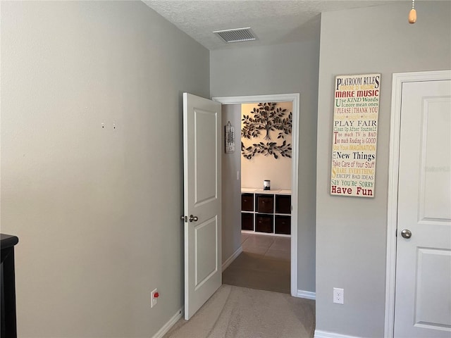 hallway with light carpet and a textured ceiling