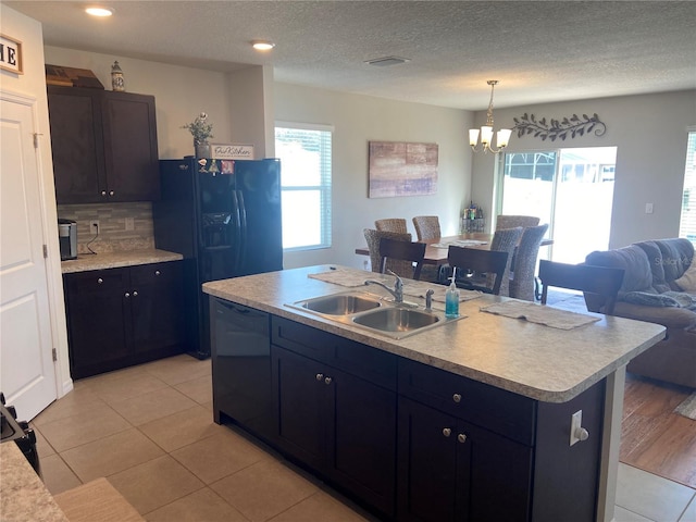 kitchen with sink, black appliances, light tile patterned floors, a center island with sink, and an inviting chandelier