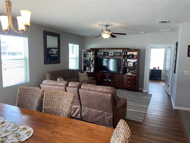 living room featuring dark hardwood / wood-style flooring, ceiling fan with notable chandelier, a healthy amount of sunlight, and a textured ceiling