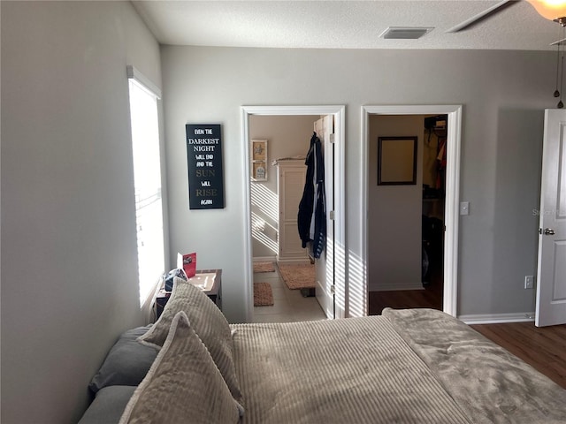 bedroom with wood-type flooring, a spacious closet, connected bathroom, and multiple windows