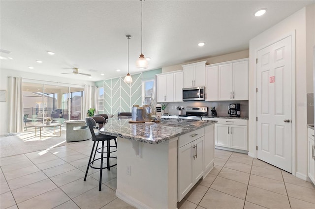 kitchen featuring ceiling fan, hanging light fixtures, stainless steel appliances, and a kitchen island with sink