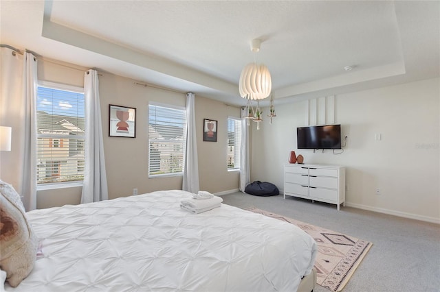 bedroom with a raised ceiling, light colored carpet, and multiple windows