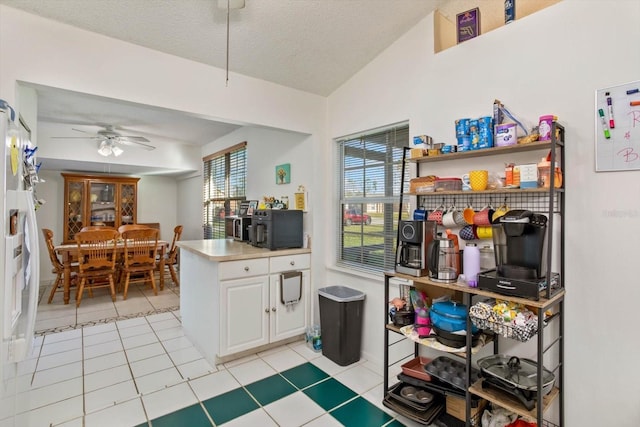 kitchen featuring a textured ceiling, ceiling fan, light tile patterned floors, white cabinetry, and lofted ceiling