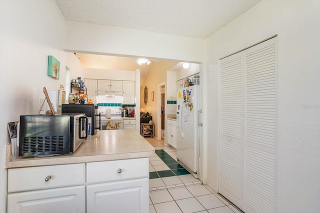 kitchen with white cabinets, a textured ceiling, white fridge with ice dispenser, and light tile patterned flooring