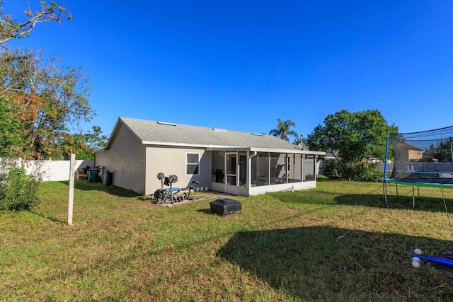 rear view of property featuring a lawn, a sunroom, and a trampoline