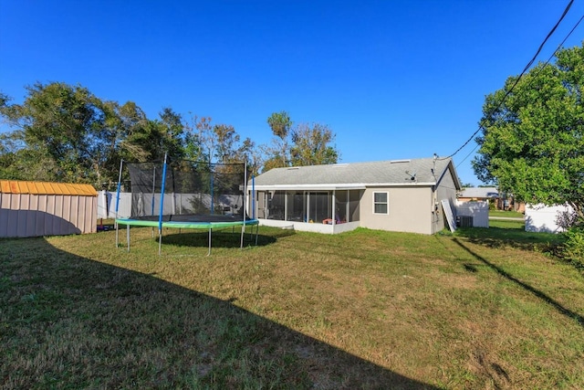 rear view of property with a sunroom, a storage unit, a trampoline, and a lawn