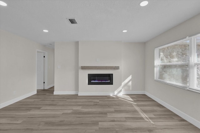 unfurnished living room with a wealth of natural light, light hardwood / wood-style floors, and a textured ceiling