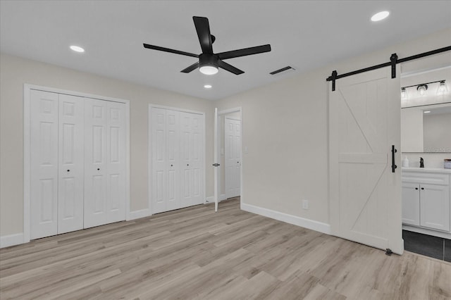 unfurnished bedroom with a barn door, ensuite bathroom, ceiling fan, and light wood-type flooring