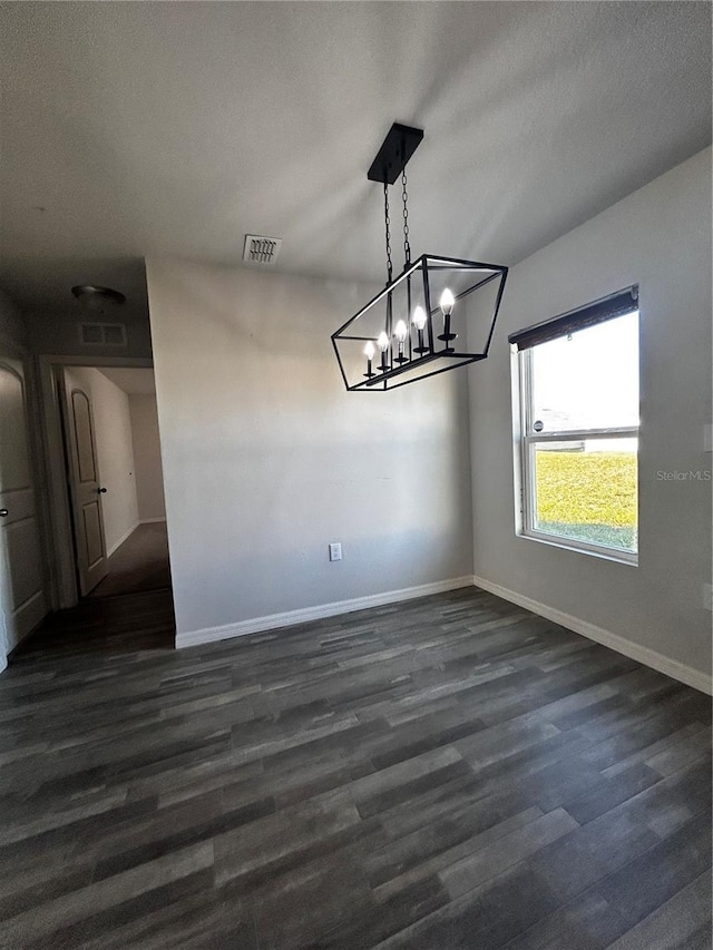 unfurnished dining area with dark wood-type flooring, a textured ceiling, and an inviting chandelier