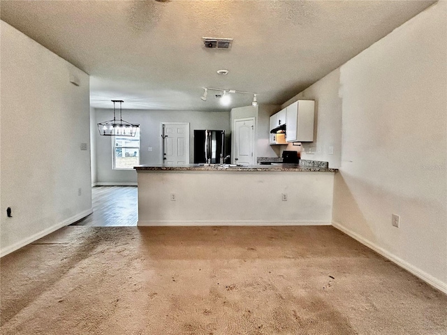 kitchen with visible vents, hanging light fixtures, freestanding refrigerator, white cabinets, and a peninsula