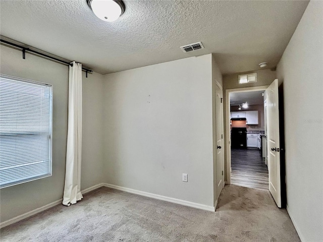 unfurnished room featuring light colored carpet, visible vents, a textured ceiling, and baseboards