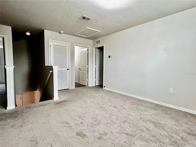 carpeted spare room with a textured ceiling, baseboards, visible vents, and attic access