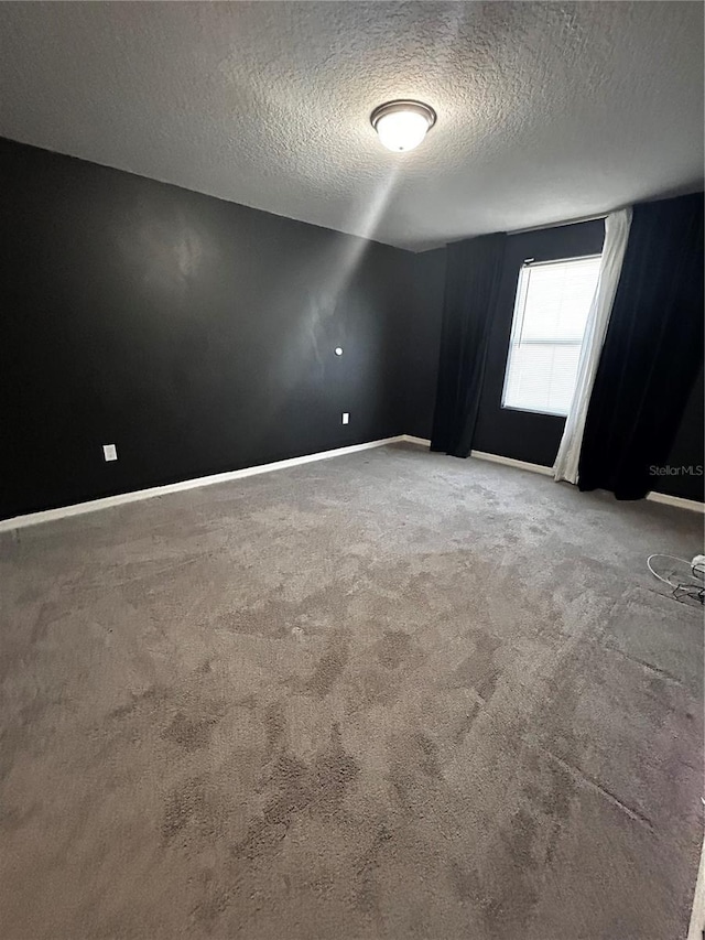 carpeted empty room featuring a textured ceiling and baseboards