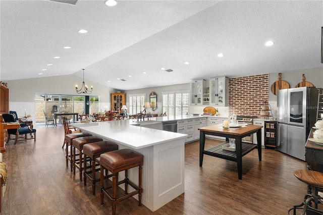 kitchen with kitchen peninsula, stainless steel fridge, vaulted ceiling, hanging light fixtures, and a breakfast bar area