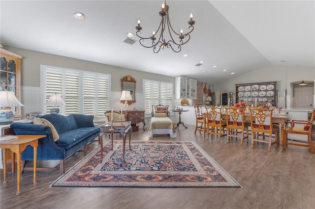 living room with hardwood / wood-style flooring, vaulted ceiling, a wealth of natural light, and a notable chandelier