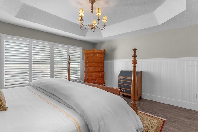 bedroom featuring a chandelier, wood-type flooring, a textured ceiling, and a tray ceiling