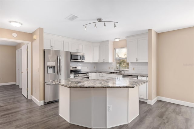 kitchen with a center island, stainless steel appliances, white cabinetry, and dark stone counters