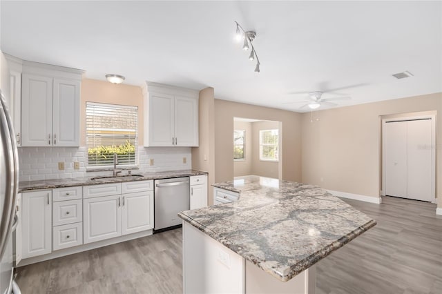 kitchen featuring light stone countertops, white cabinets, sink, dishwasher, and a center island